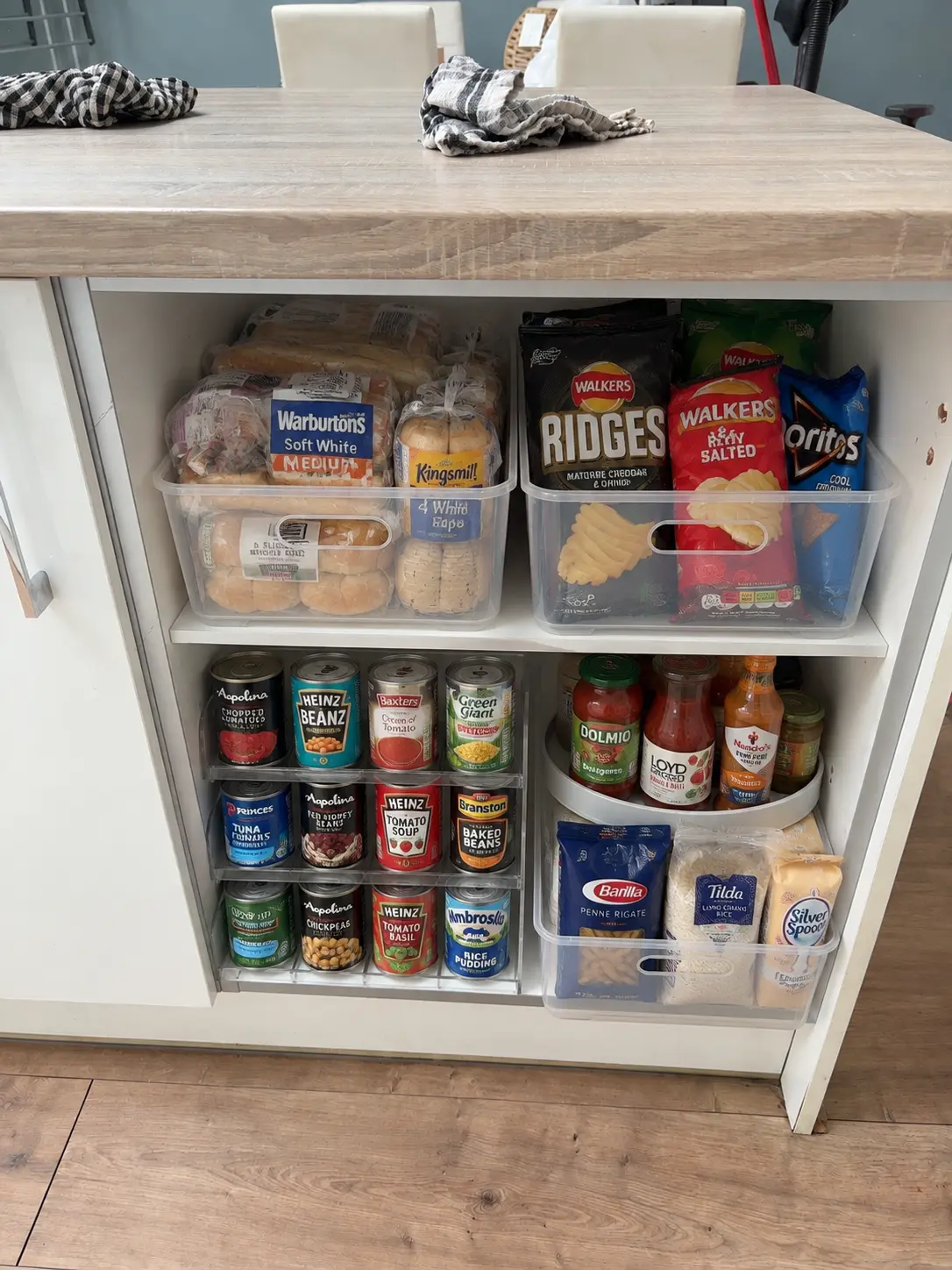 The same food cupboard organised with clear bins, a tiered tin riser and a turntable