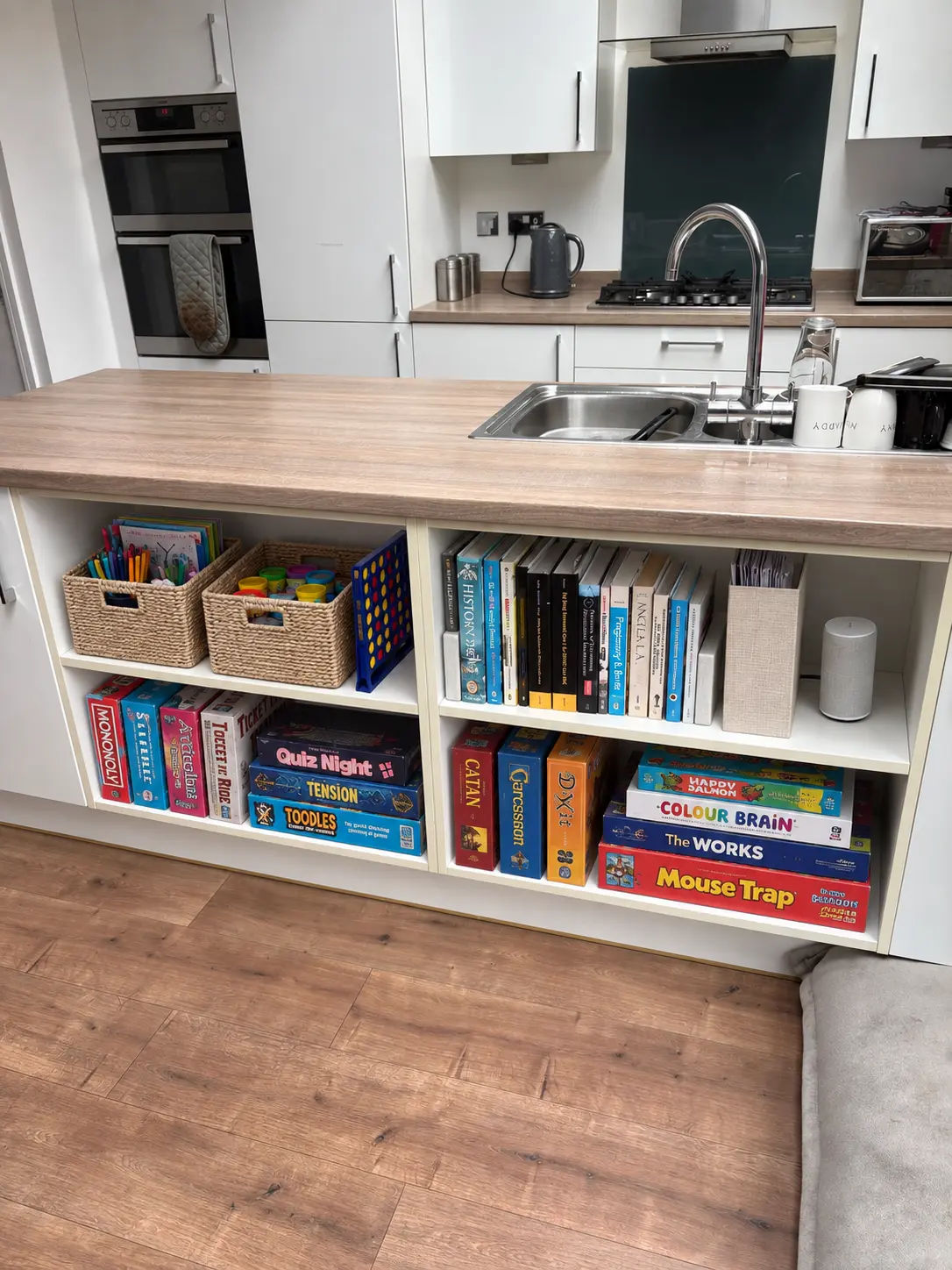 The same kitchen shelves organised with baskets, upright games, books and a file holder
